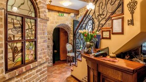A reception area with a wooden counter, a telephone, a vase with flowers, and a stone wall with a fireplace. - Hotel Monte Cristo (Kotor)