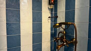 A bathroom with blue and white tiles, a shower with a brass faucet, and a bottle of cleansing gel on the wall.