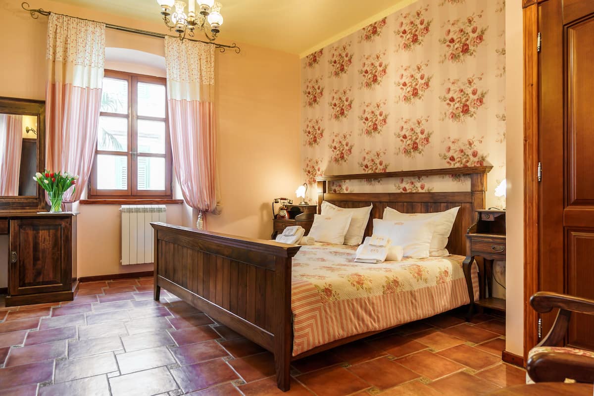 A bedroom with a wooden bed, floral wallpaper, a radiator, and a window with curtains.