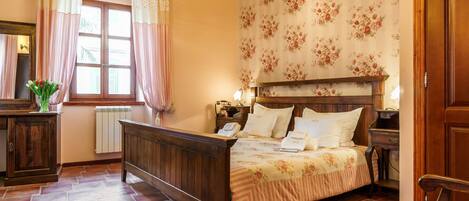 Un dormitorio con cama de madera, papel tapiz floral, un radiador y una ventana con cortinas.