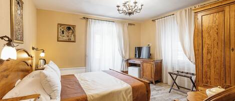 Ett hotellrum med en säng, ett sängbord, en lampa, en garderob i trä och ett skrivbord med en stol.