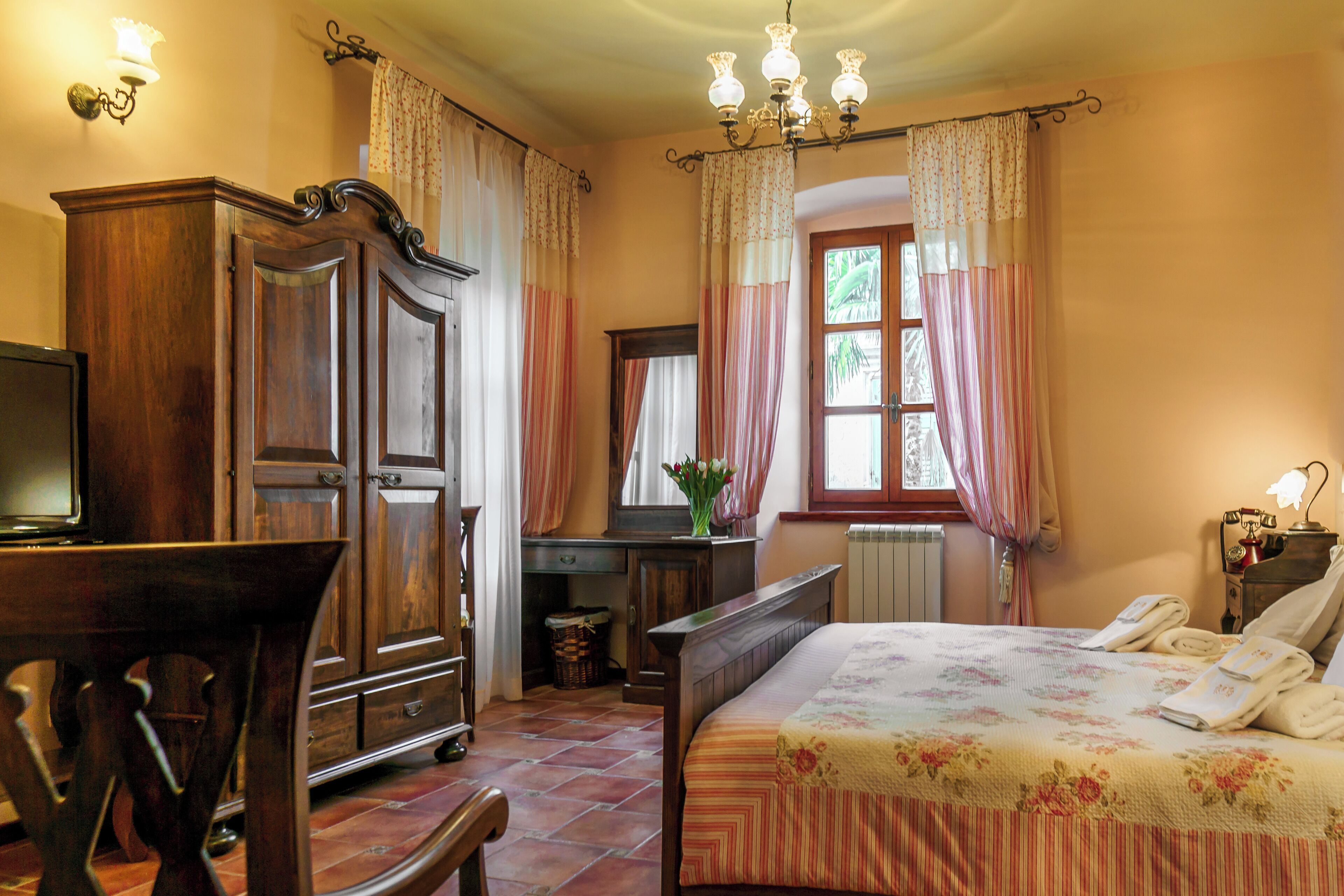 Un dormitorio con cama de madera, un escritorio, una silla, un televisor y una ventana con cortinas.