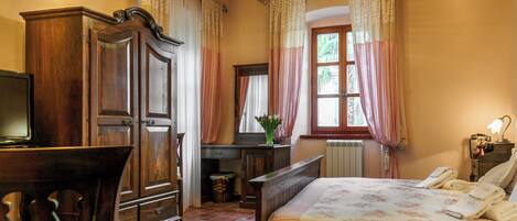 Un dormitorio con cama de madera, un escritorio, una silla, un televisor y una ventana con cortinas.