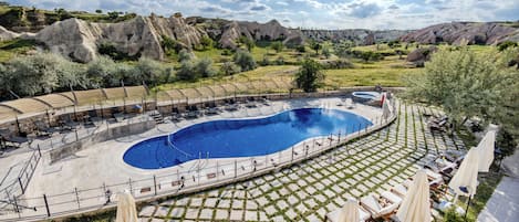 Zona de piscina con sillones reclinables y sombrillas, rodeada de terreno rocoso y vegetación.