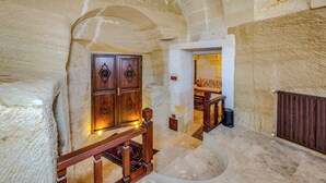 Interior de piedra con una escalera de madera, una puerta con tallas intrincadas y una pequeña alfombra en el suelo.