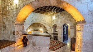 Una habitación con paredes de piedra, una cama, un banco de madera y un florero.