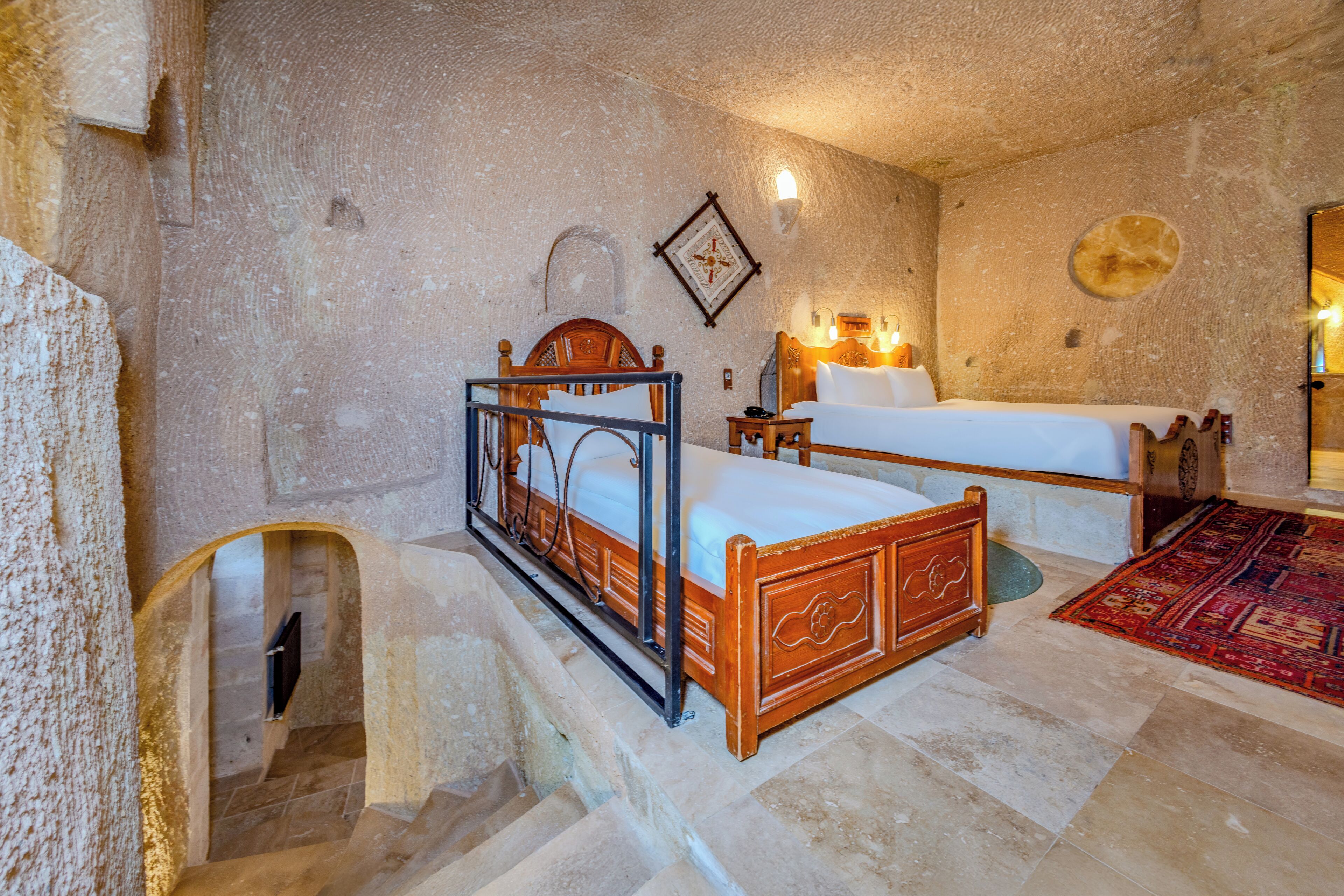 A room with a wooden bed, a second bed, a small table, and a wall-mounted light fixture.