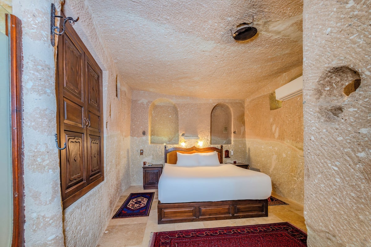 A bedroom with a wooden bed, a nightstand, a mirror, and a stone wall.