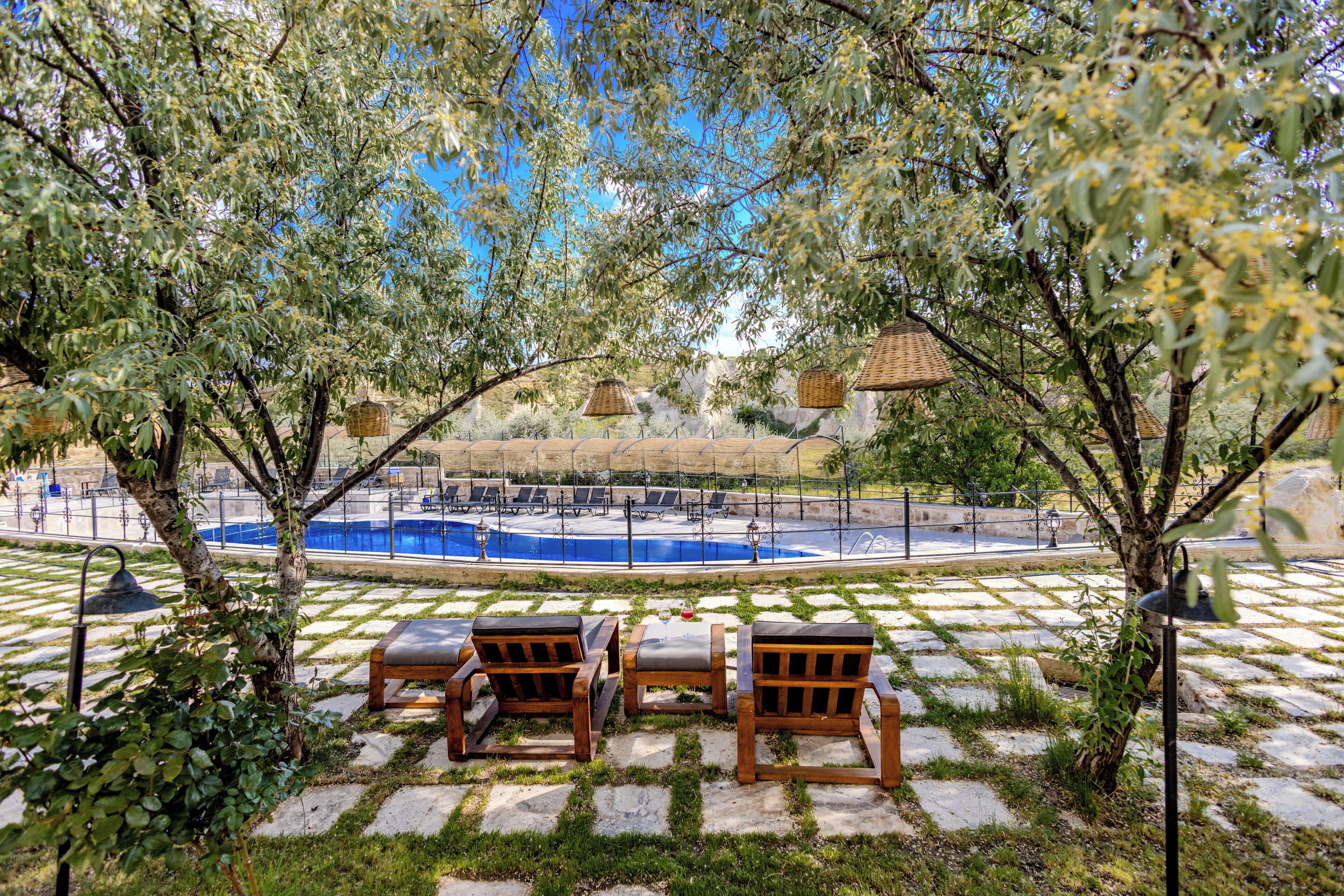 Zona junto a la piscina con sillones de descanso, una piscina y una pérgola con cestas colgantes.