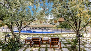 Zona junto a la piscina con sillones de descanso, una piscina y una pérgola con cestas colgantes.