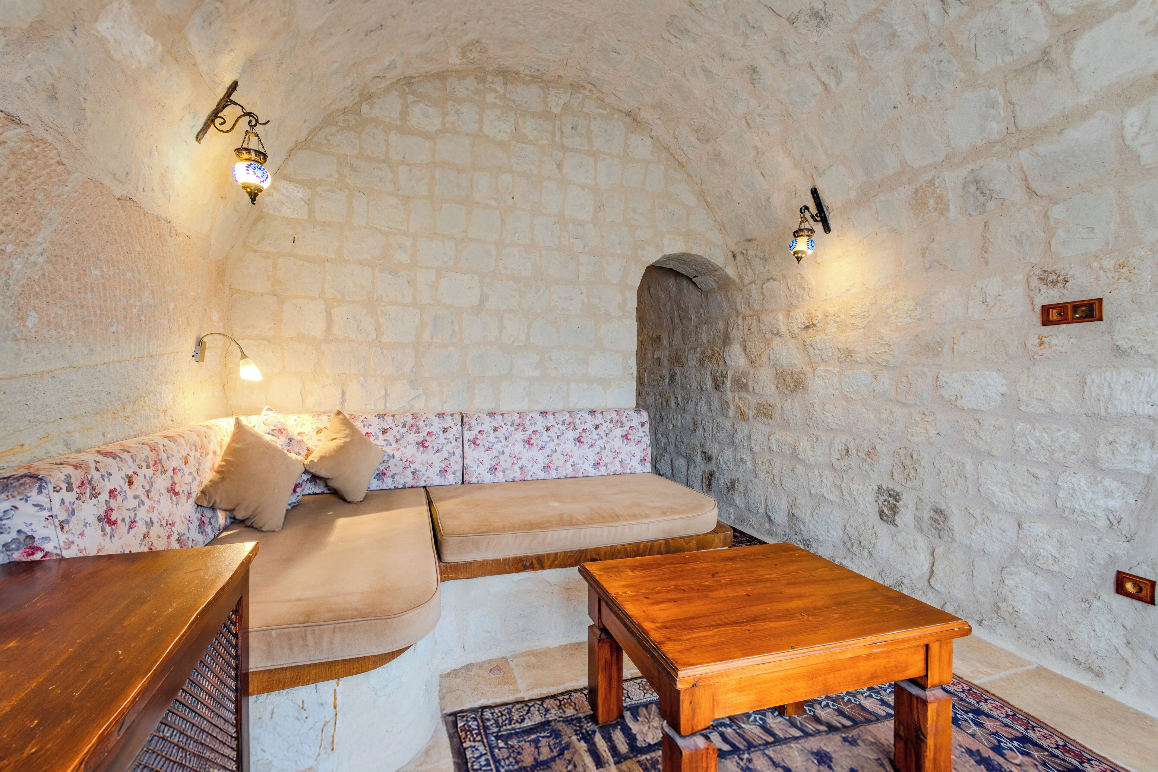 A cozy room with a stone wall, a wooden bench, a cushioned bench, and a small table.