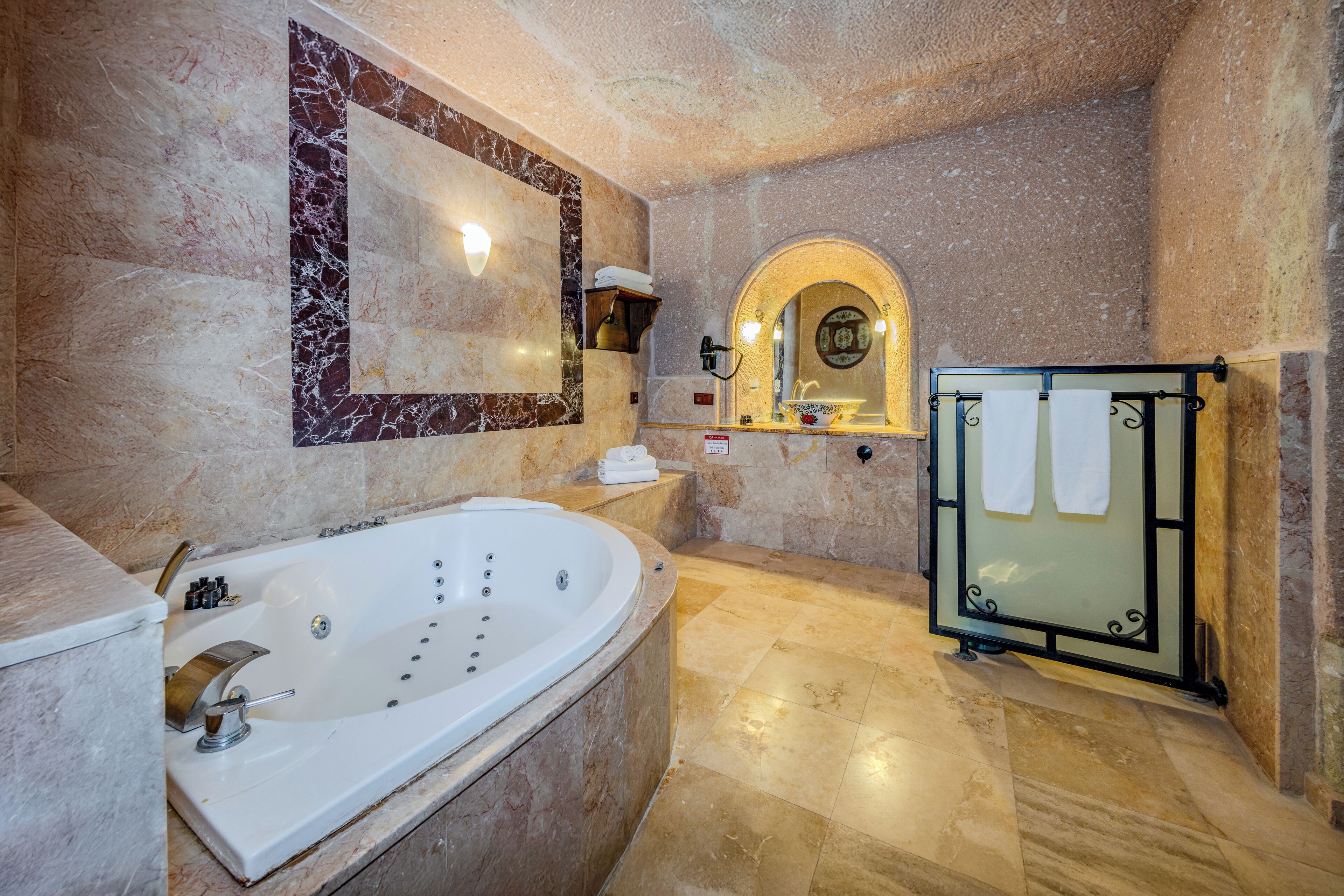 A bathroom with a large bathtub, a glass shower enclosure, marble walls, and a built-in sink.
