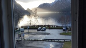 A view from a window overlooking a parking area with a lake and mountains in the background. - Trolltunga Hotel (Ullensvang)