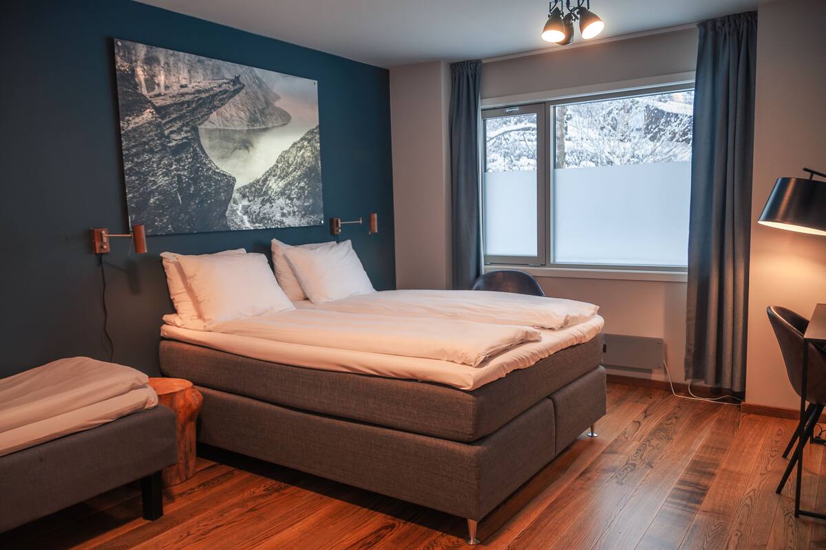 A bedroom with a large bed, a desk, a chair, and a window with a view of snow-covered mountains.