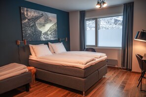 A bedroom with a large bed, a desk, a chair, and a window with a view of snow-covered mountains.