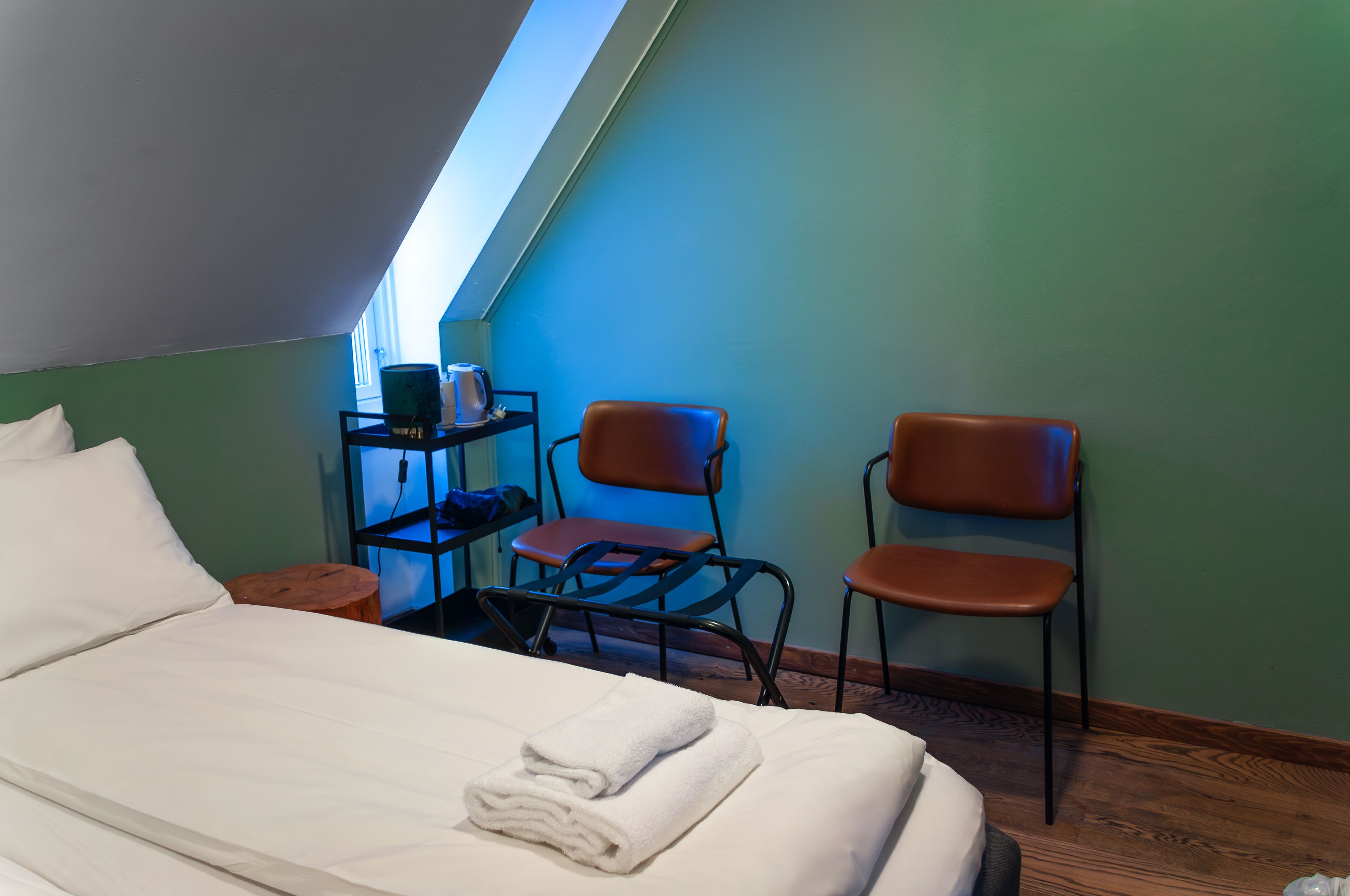 Een slaapkamer met een bed, twee stoelen, een klein tafeltje en een plank met een waterkoker.