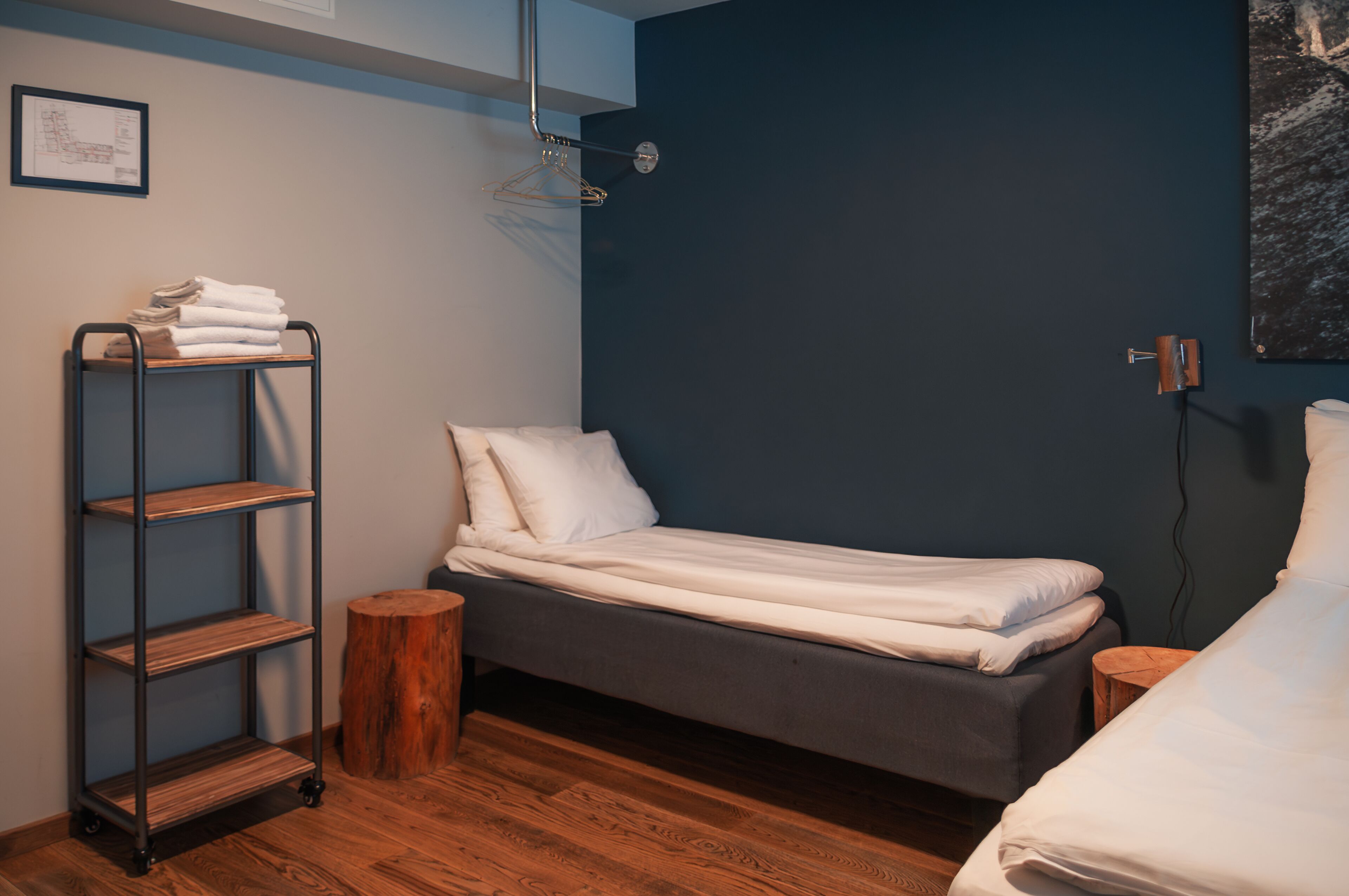 A small, neatly arranged bedroom with a single bed, a wooden shelf unit, and a small wooden stool.