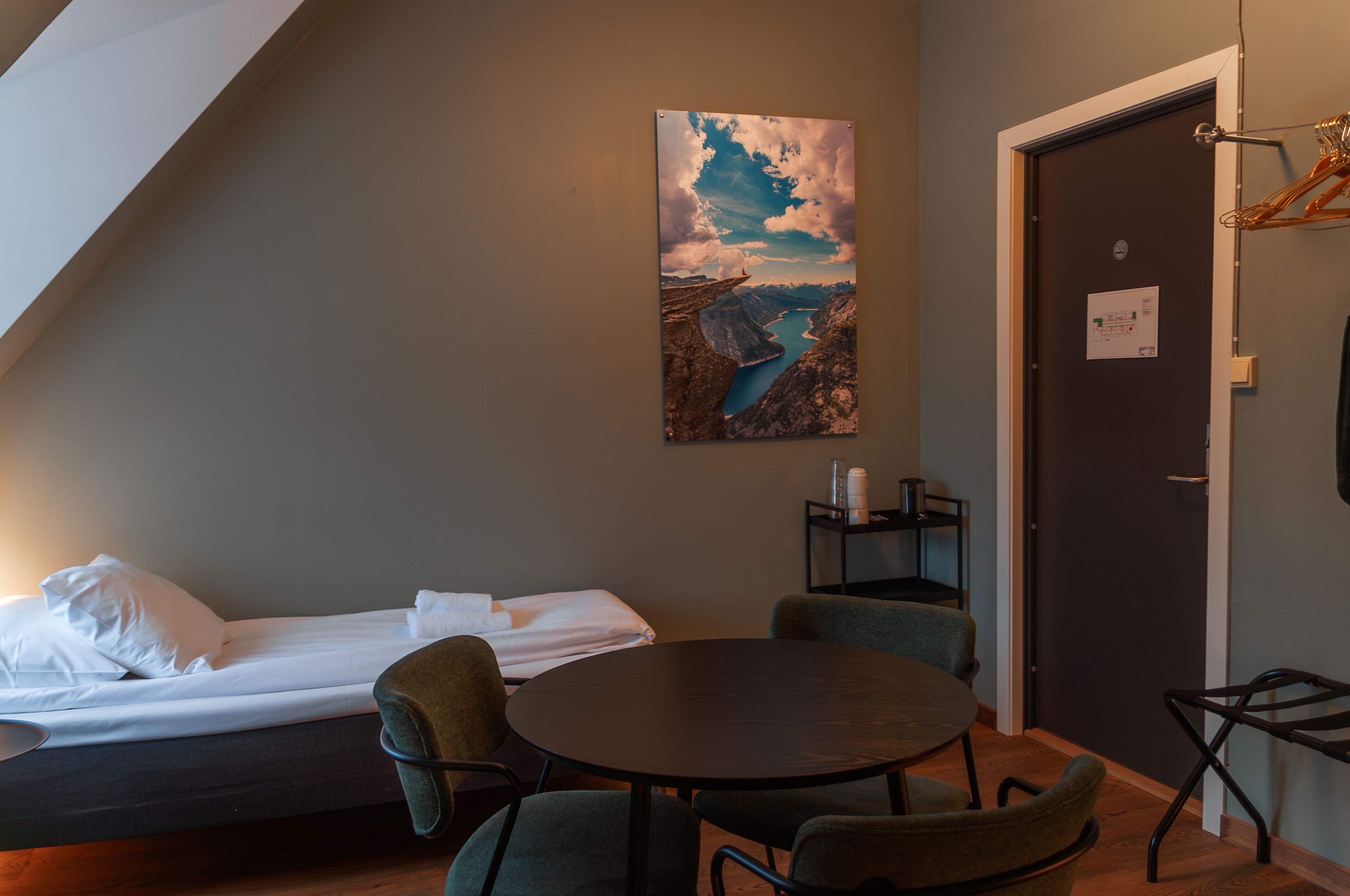 Une pièce comprenant un lit, une table ronde et des chaises, un tableau représentant un paysage accroché au mur, et une porte avec une pancarte.