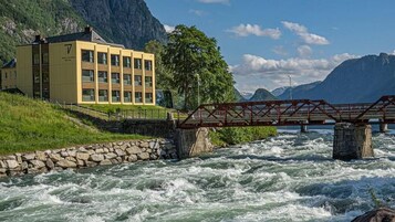 A hotel with a yellow facade, a stone retaining wall, and a bridge over a fast-flowing river.