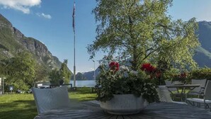 A wooden table with a potted plant in the center, surrounded by chairs, set against a backdrop of mountains and a body of water. - Trolltunga Hotel (Ullensvang)