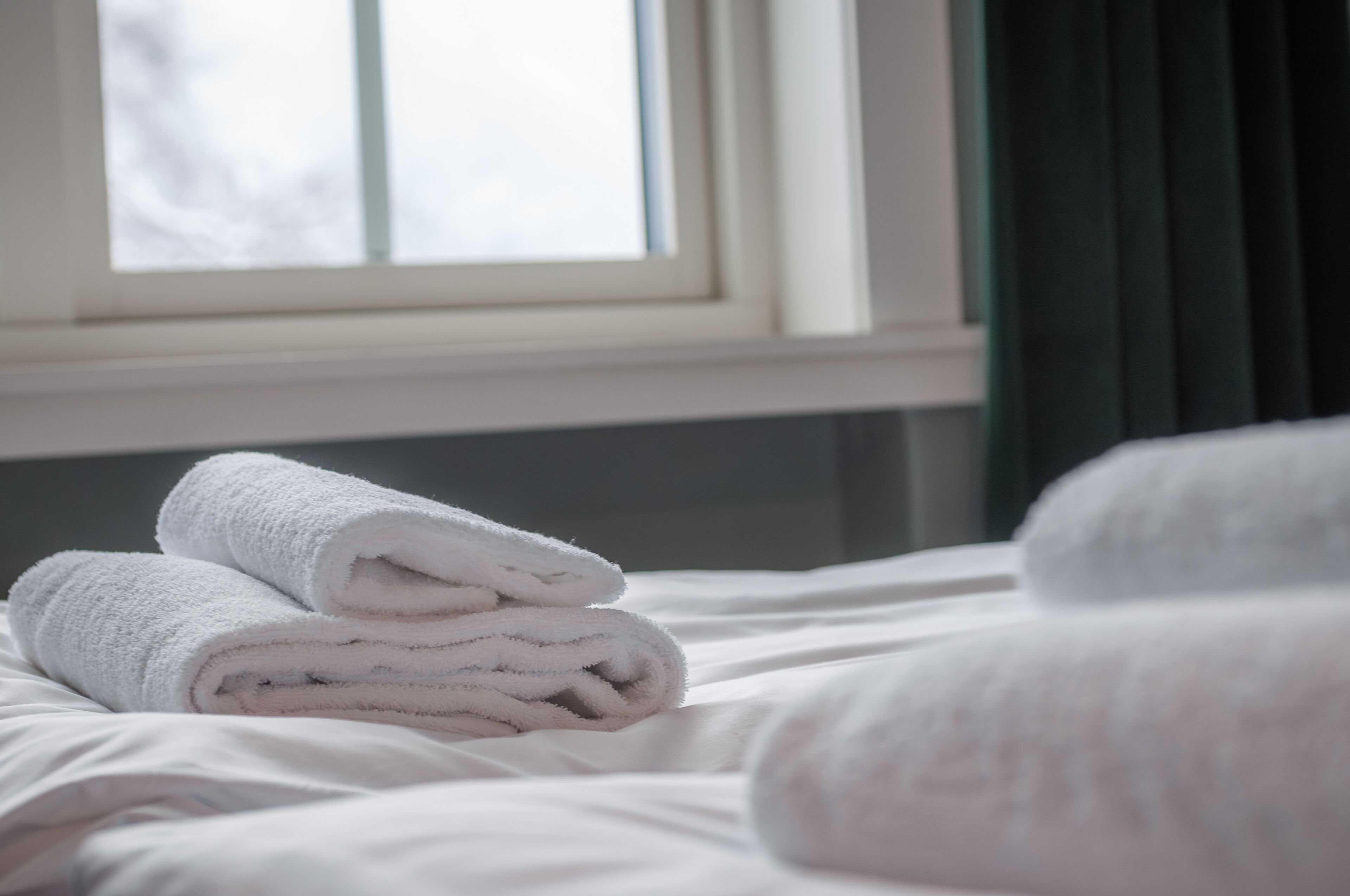 Een net opgemaakt bed met witte lakens en opgerolde handdoeken.