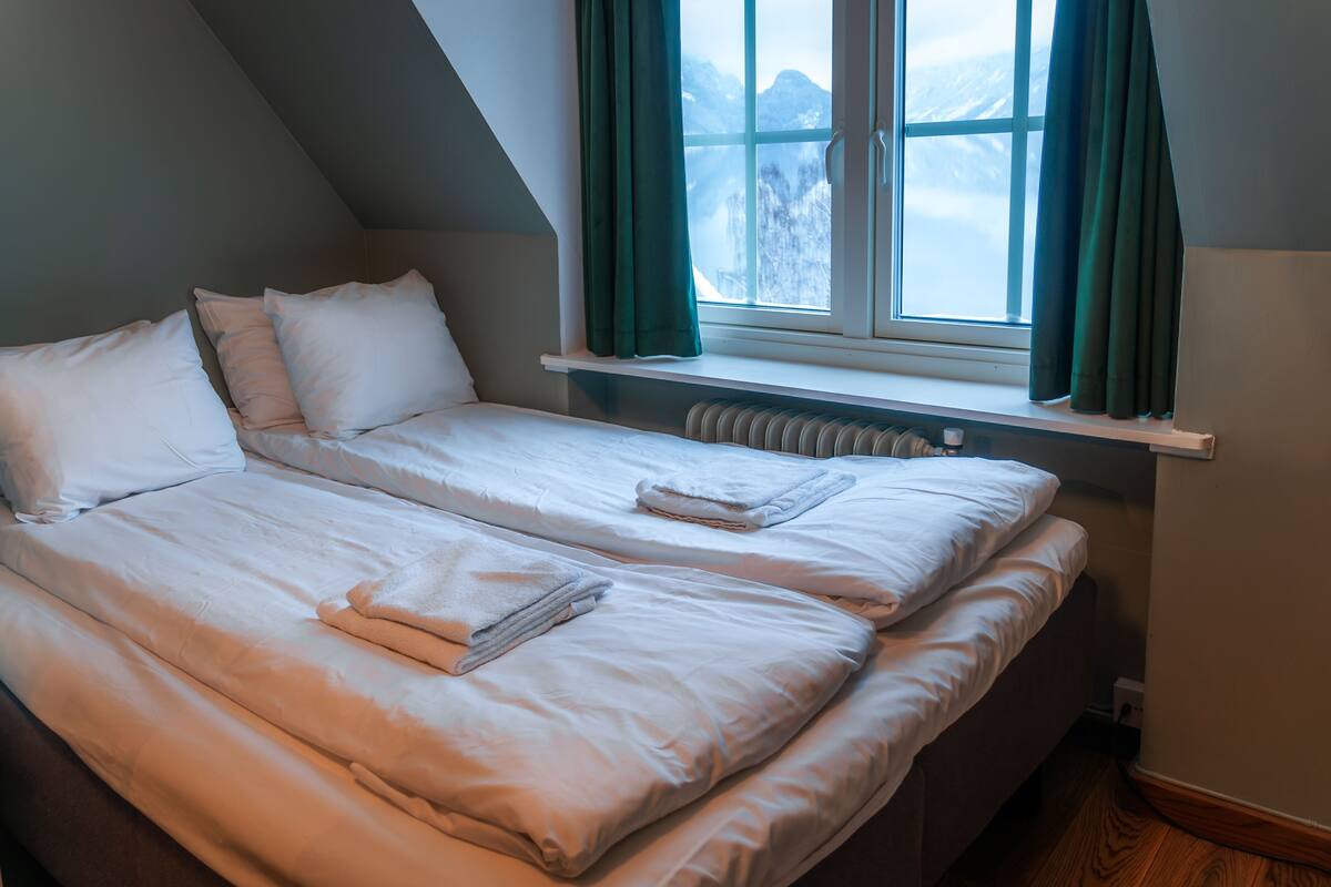 A room with two beds, a window with curtains, and a radiator.