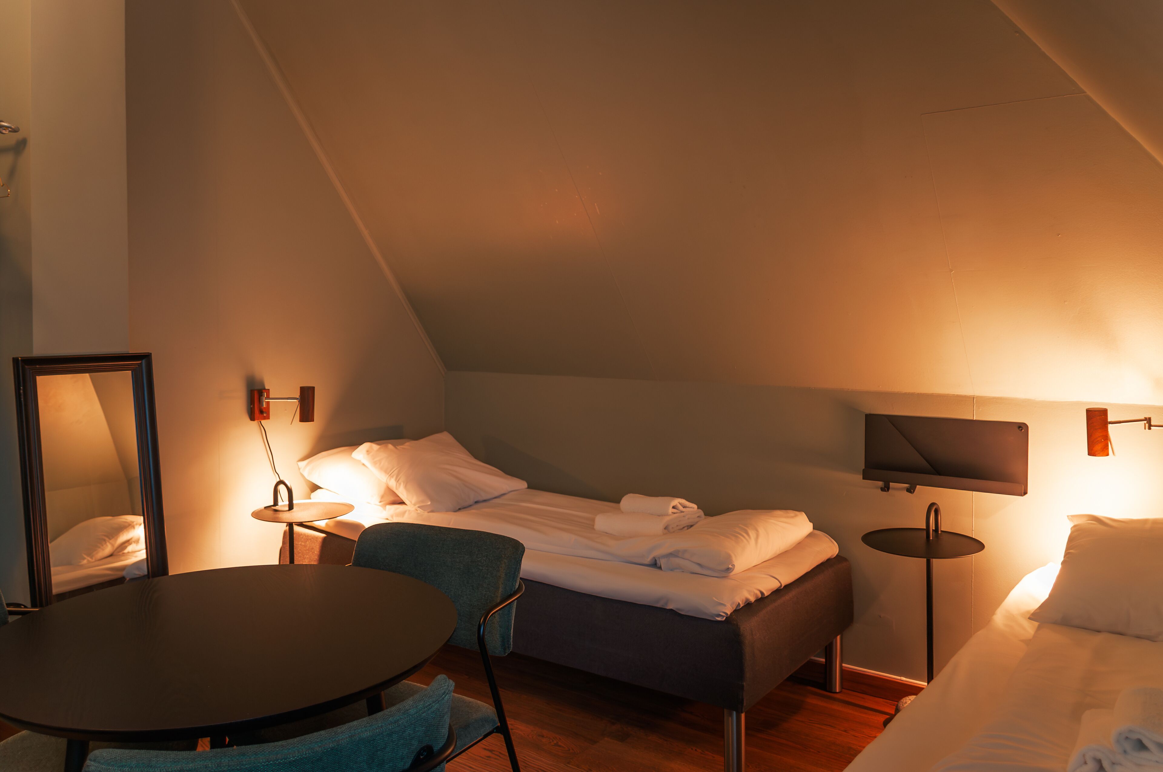 Une pièce confortable et bien éclairée, avec un lit, une table ronde, une chaise, une petite table ronde et un téléviseur fixé au mur.