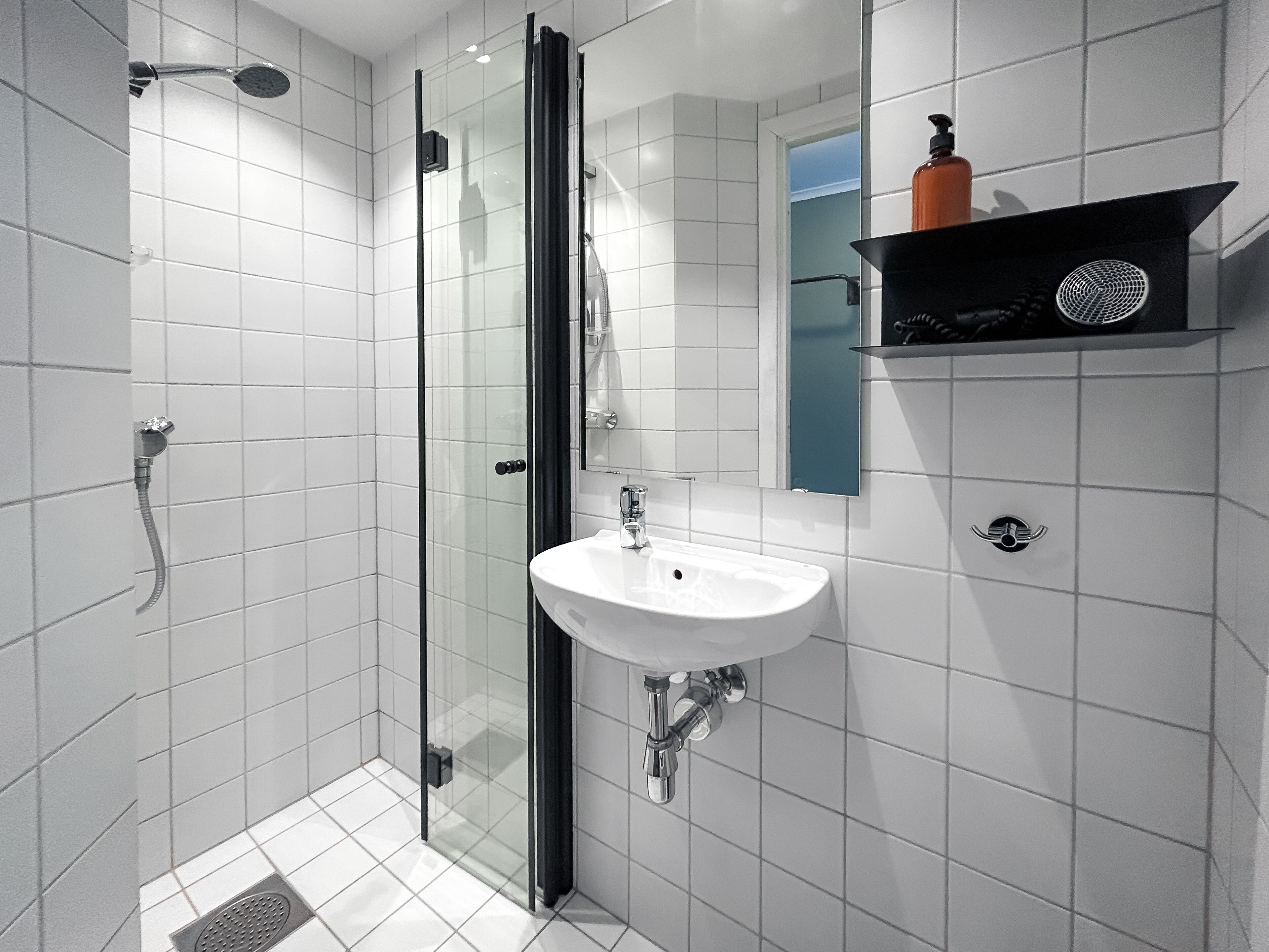 A modern bathroom with a glass-enclosed shower, a white sink, and a mirror above it.