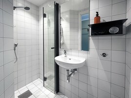 Et moderne badeværelse med et glasafskærmet brusebad, en hvid vask og et spejl over den.