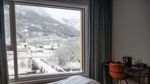A hotel room with a large window offering a view of a snowy mountain and a town below. - Trolltunga Hotel (Ullensvang)