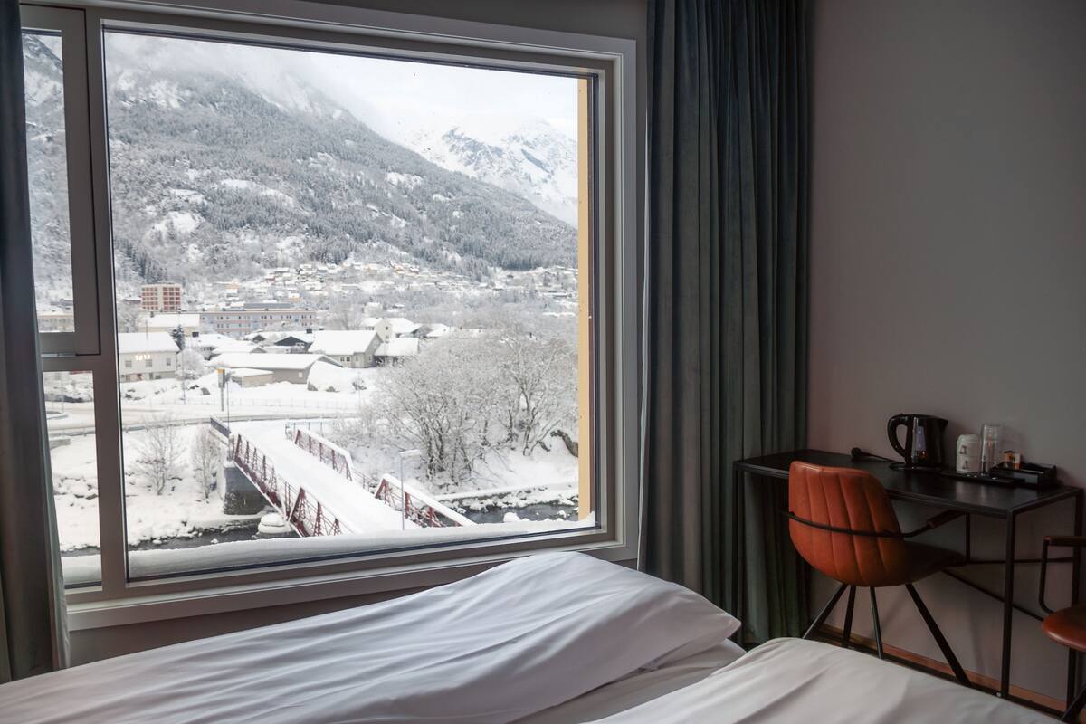 A hotel room with a large window offering a view of a snowy mountain and a town below.
