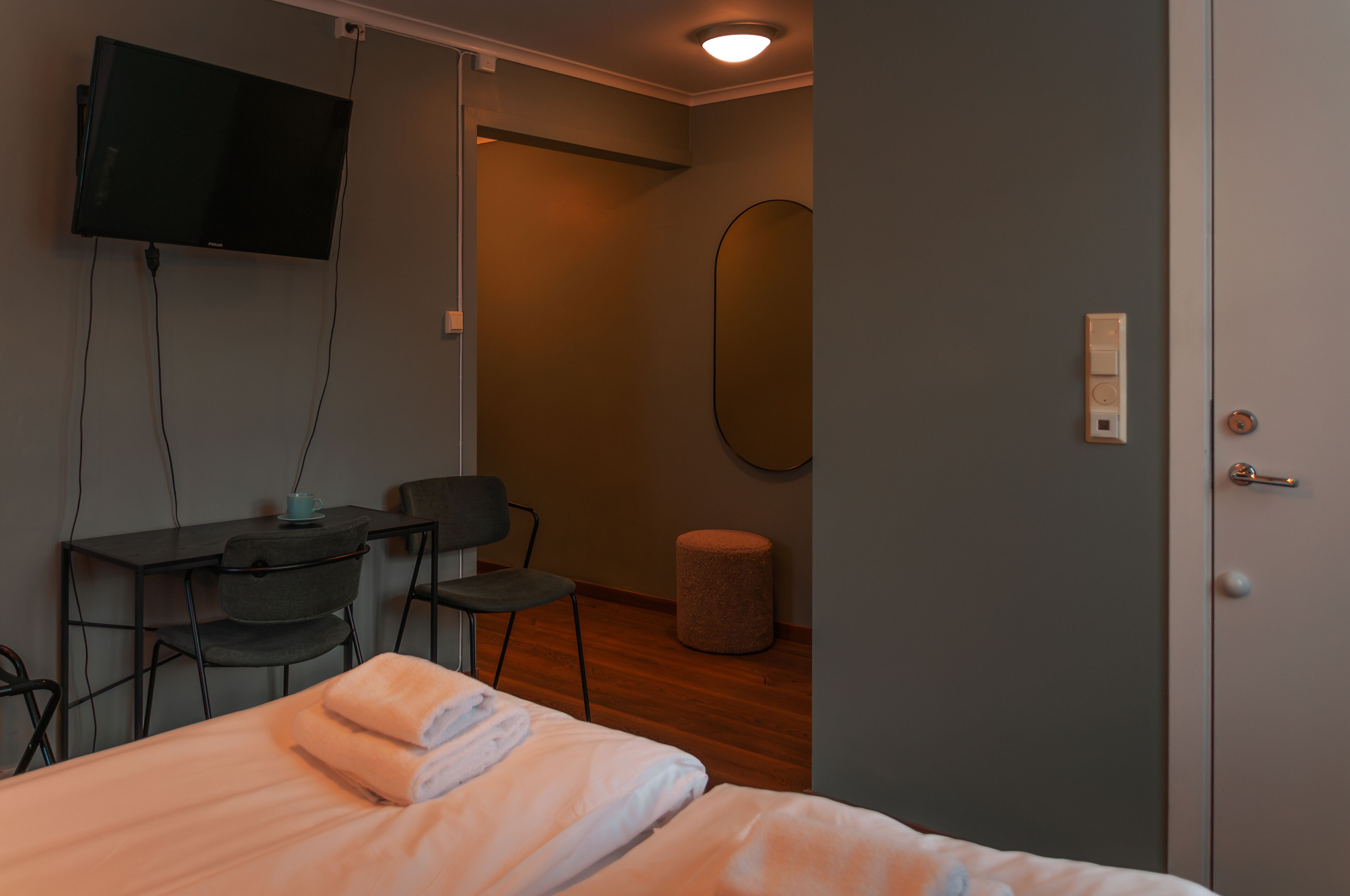 A hotel room with a bed, a desk, a chair, a television, a mirror, and a door.