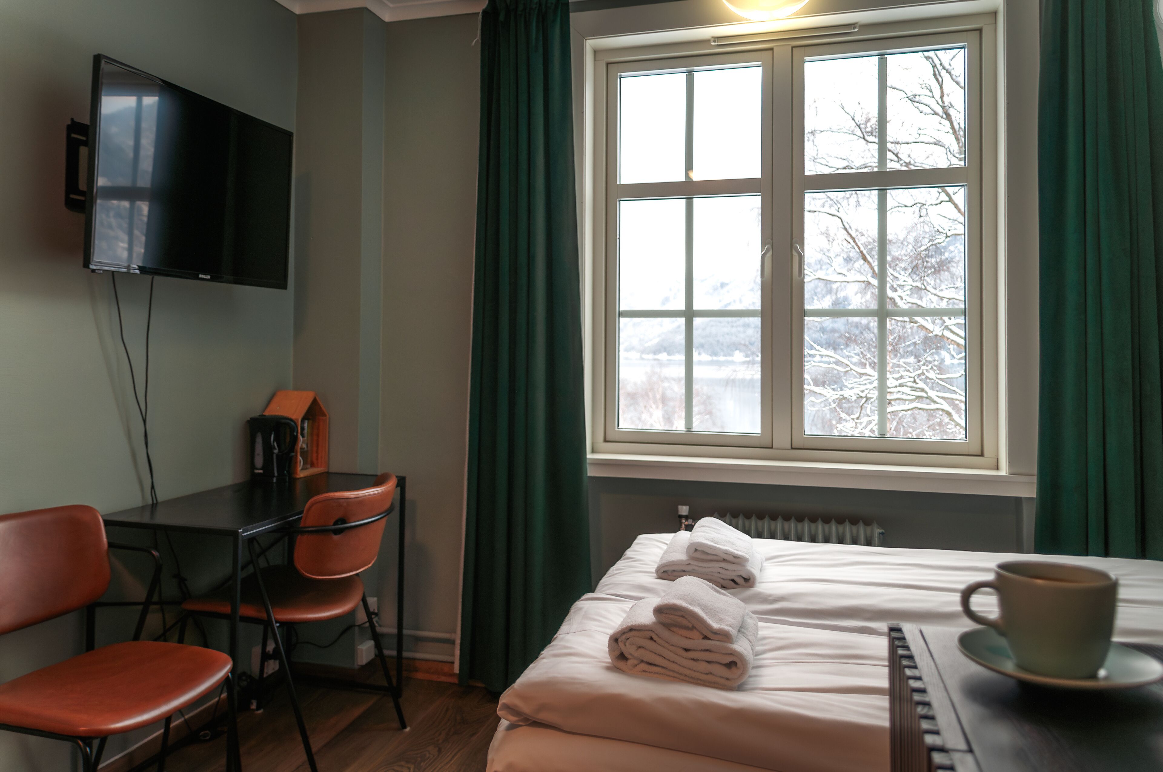 Una habitación de hotel con cama, escritorio, silla, televisor y ventana con cortinas.