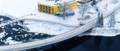 A snow-covered landscape with a bridge over a river, buildings, and a yellow structure.