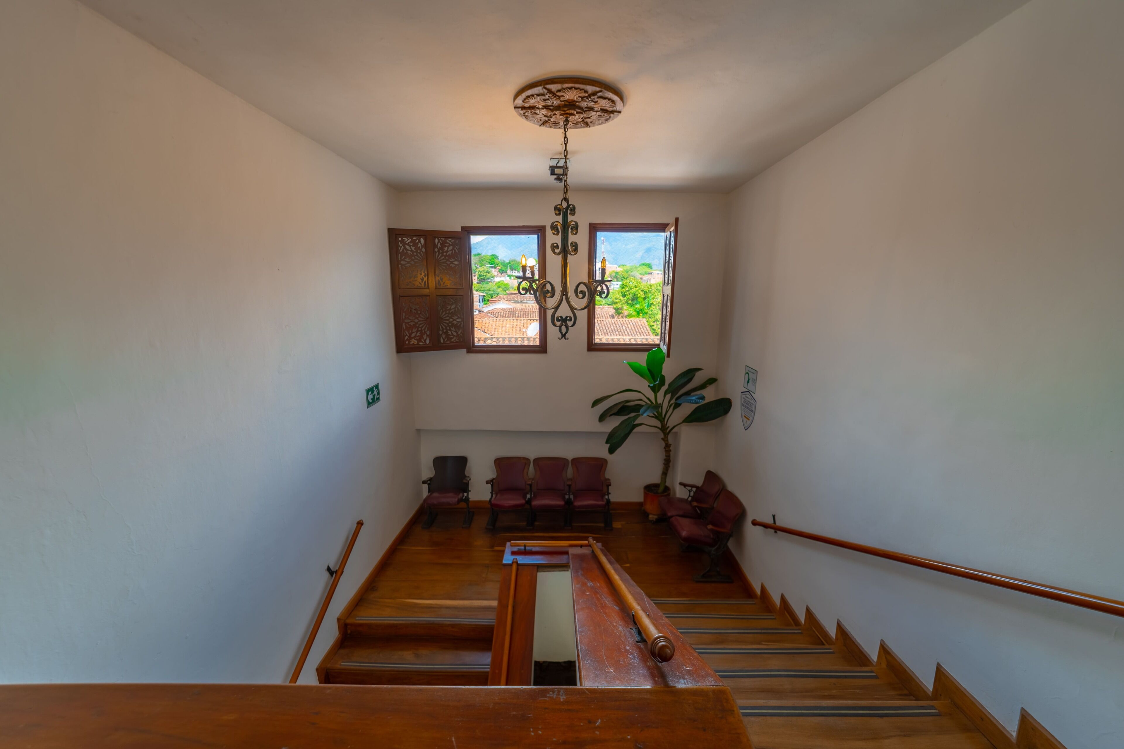 A staircase with wooden steps and a handrail, leading to a landing with red chairs and a potted plant.
