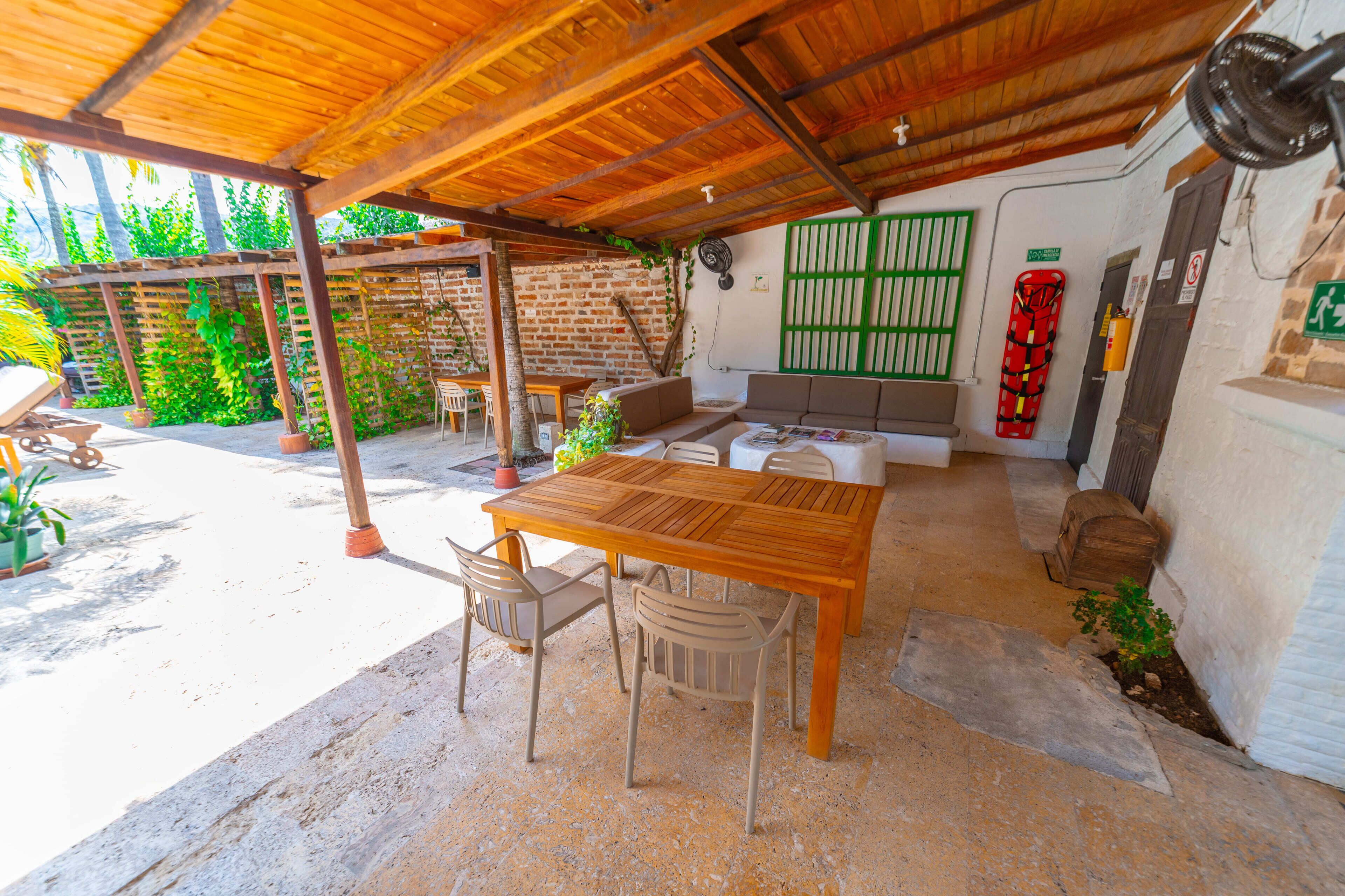 An outdoor patio with a wooden table and chairs, a sofa, and a brick wall with a green gate.
