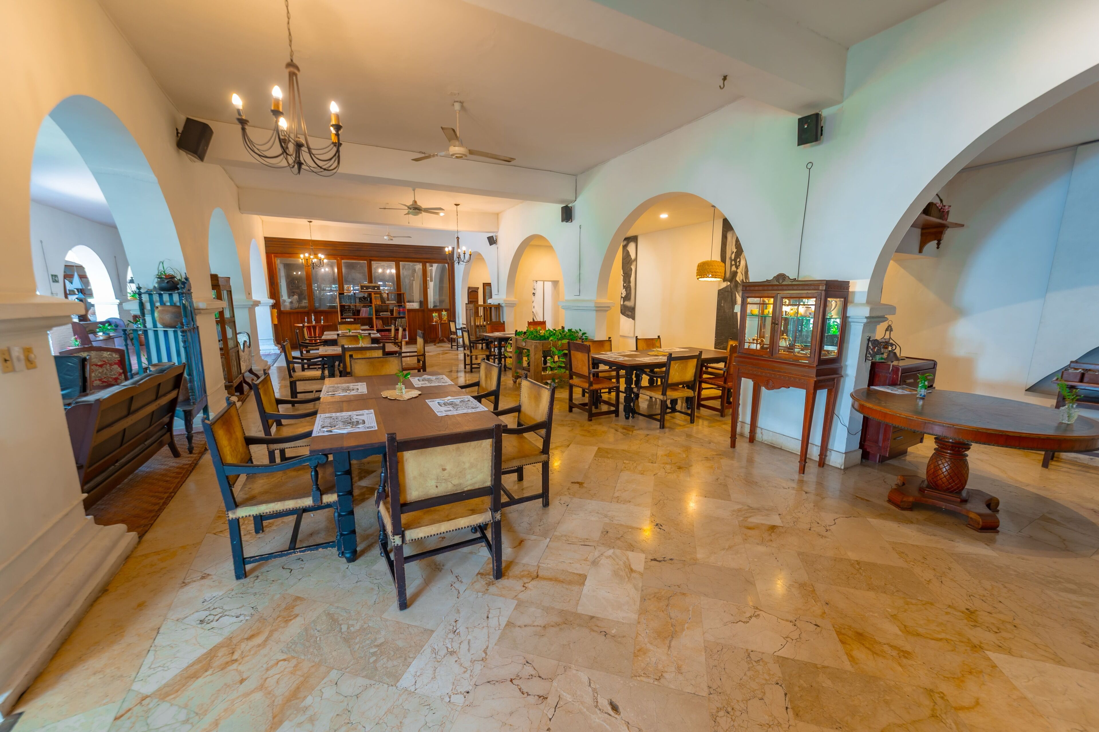 A spacious dining area with marble flooring, wooden tables and chairs, and a chandelier.