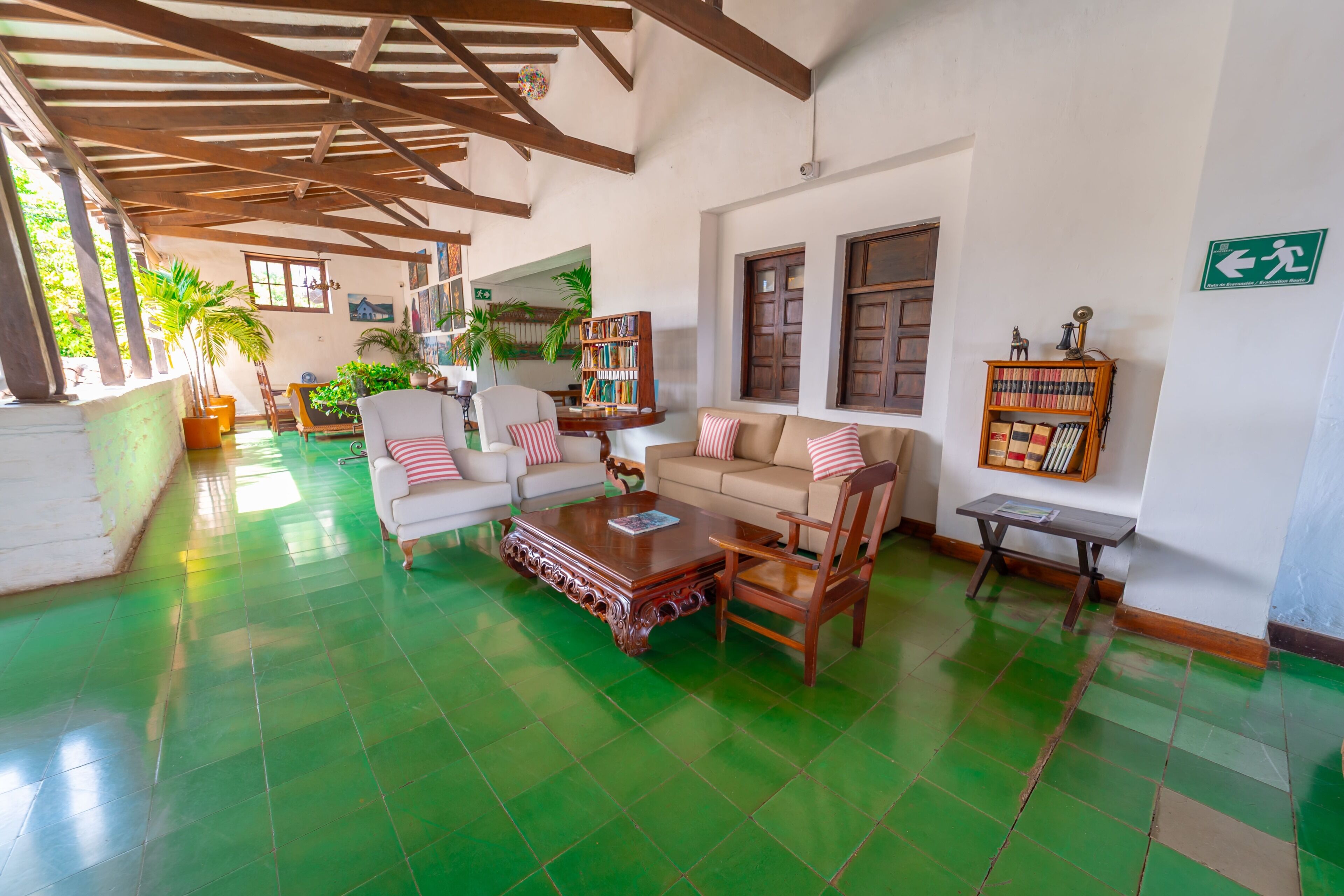 A spacious living area with a green tiled floor, wooden furniture, and a bookshelf.