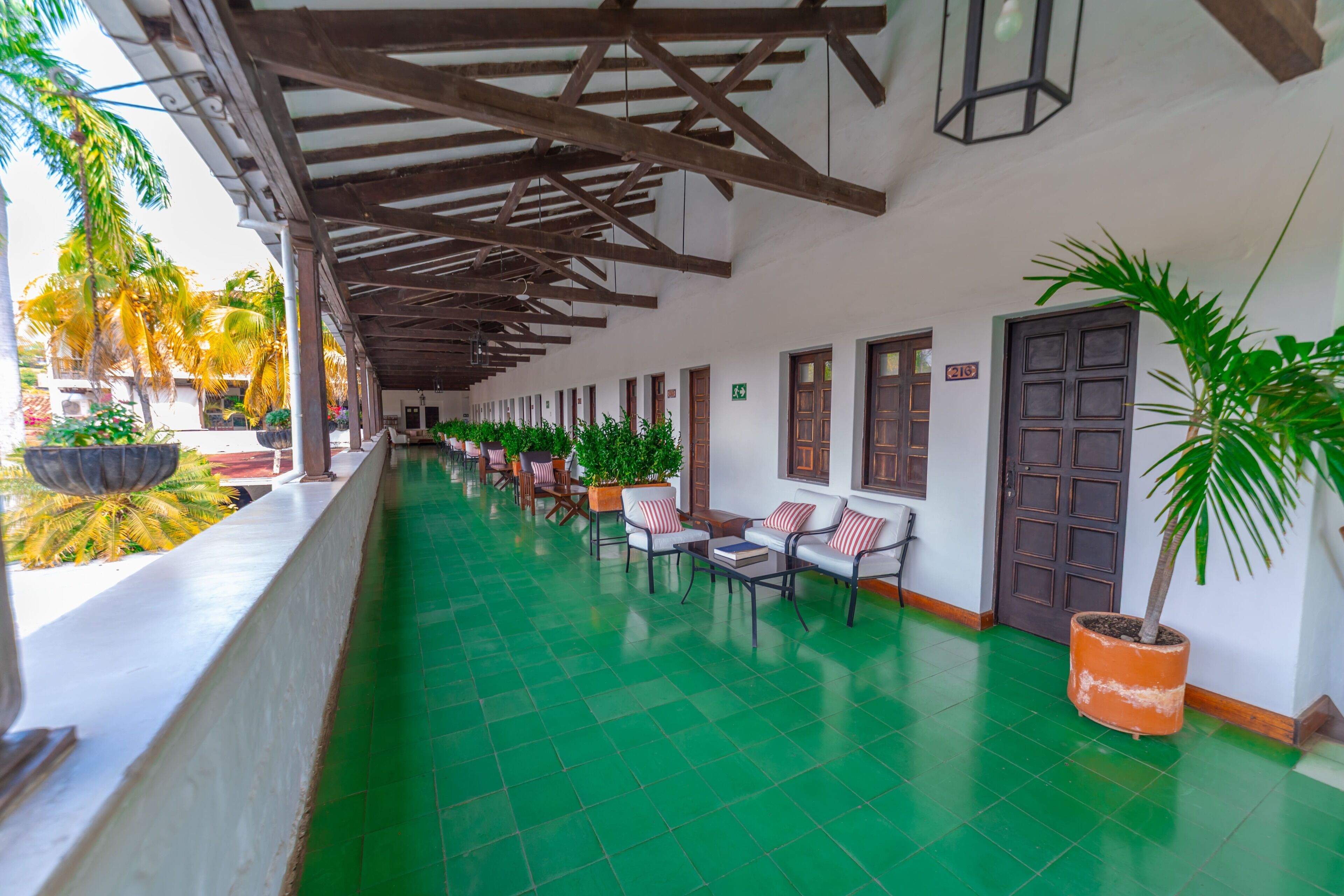 A covered corridor with green flooring, wooden beams, and potted plants.