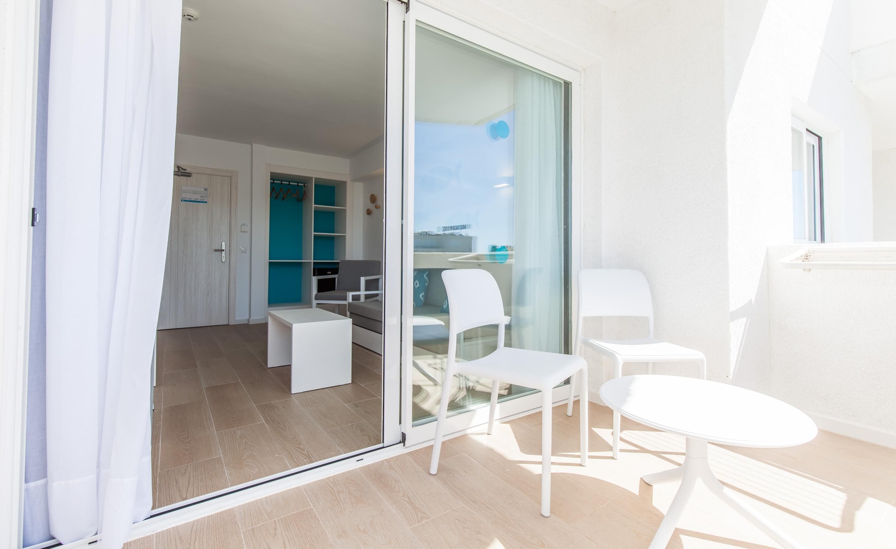 Un appartement moderne doté d’un balcon, d’une porte-fenêtre coulissante, d’une petite table blanche et d’un coin salon avec des chaises.