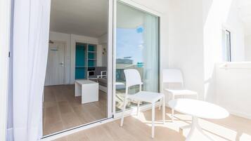 Un appartement moderne doté d’un balcon, d’une porte-fenêtre coulissante, d’une petite table blanche et d’un coin salon avec des chaises.