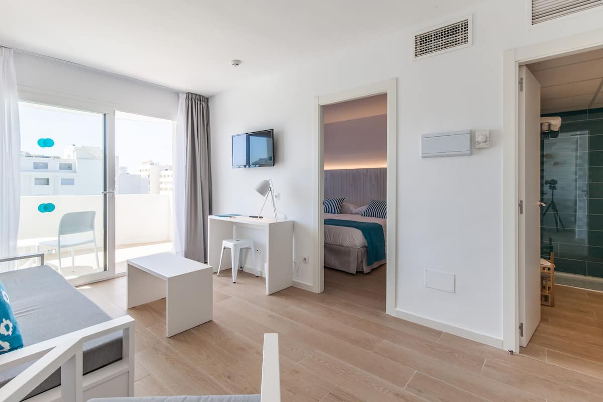 A modern hotel room with a balcony, a desk, a bed, and a TV.