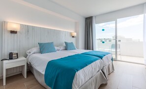 Habitación de hotel con cama, mesita de noche con teléfono y vista al cielo a través de un ventanal grande.