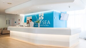A hotel reception desk with a blue and white color scheme, a digital screen, and a reception area with a sofa and a coffee table. - BLUESEA Gran Playa (Sant Llorenc des Cardassar)