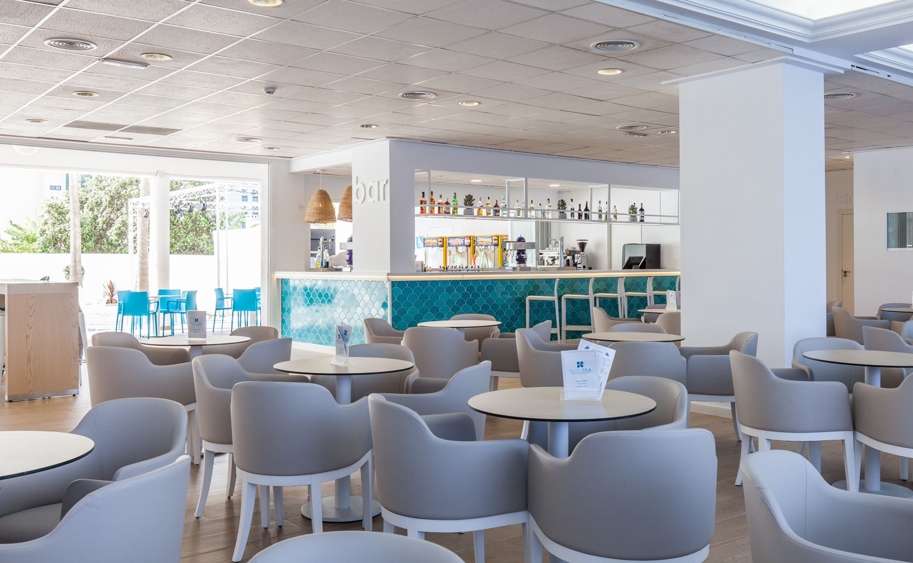 Een modern café met ronde tafels en stoelen, een bar met flessenrekken, en uitzicht op groen.