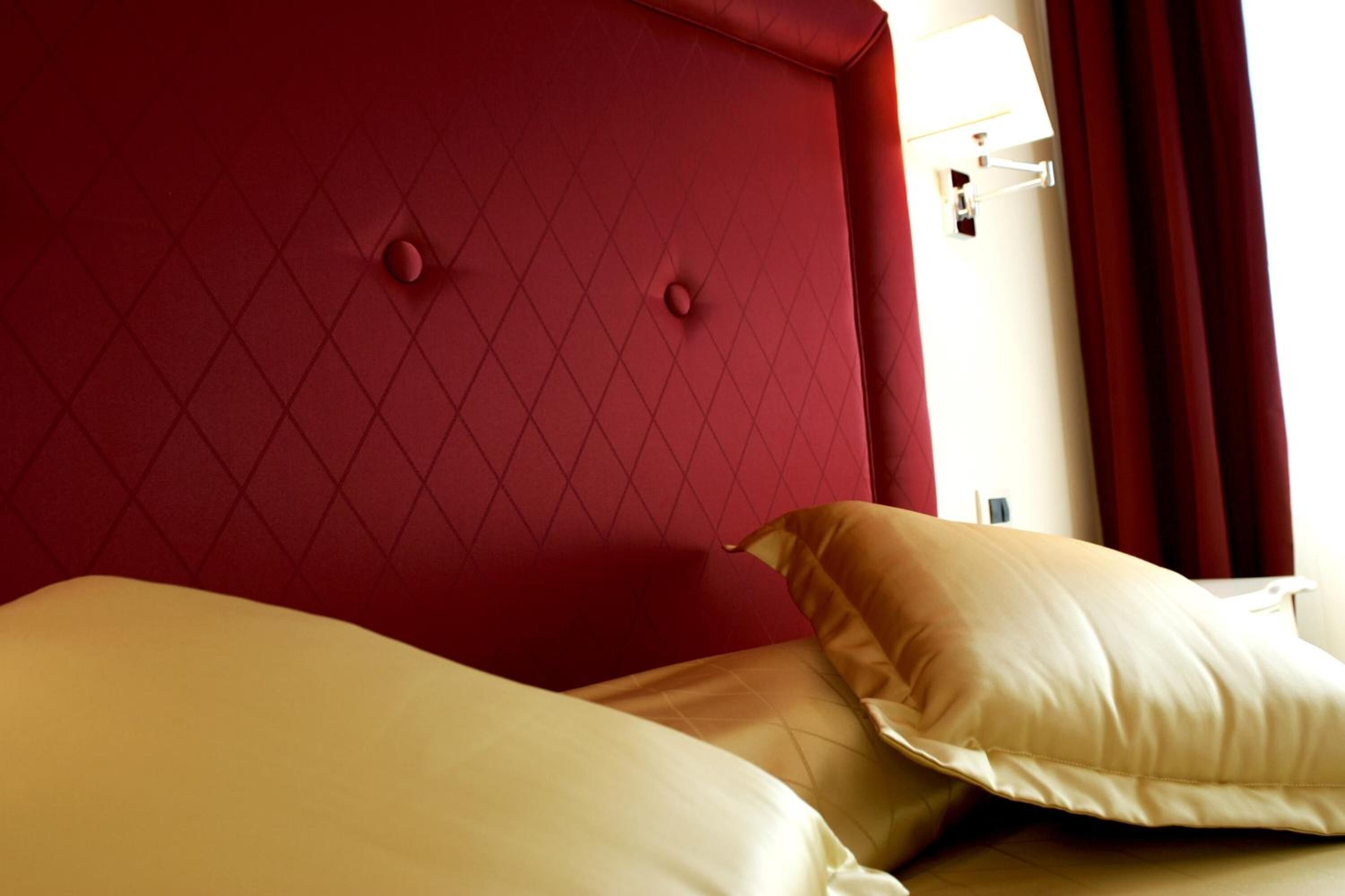A hotel room with a red headboard, two beige pillows, and a white wall with a light switch.
