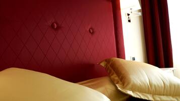 A hotel room with a red headboard, two beige pillows, and a white wall with a light switch.