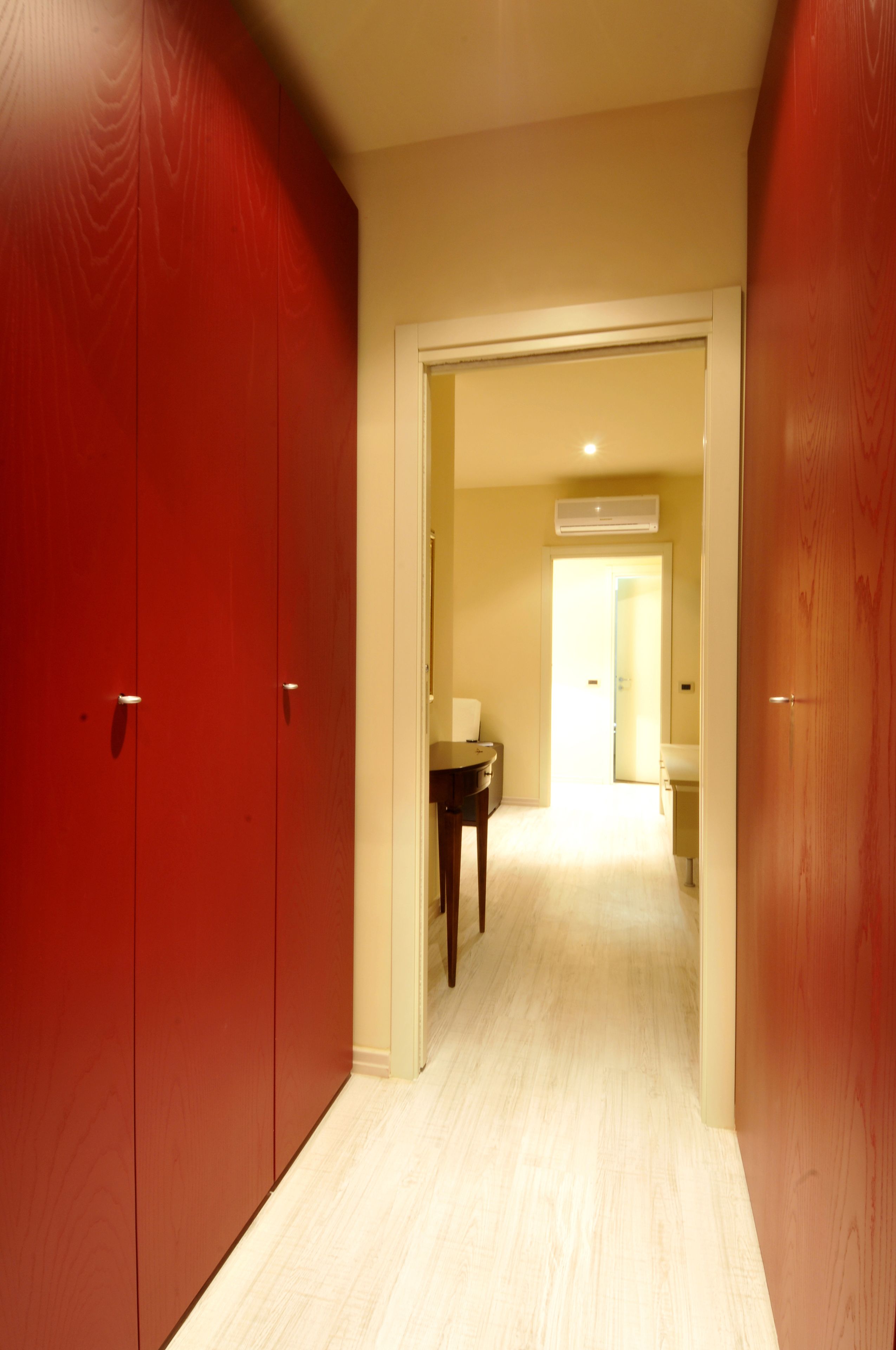A hallway with a wooden floor leading to a room with a bed and a nightstand.
