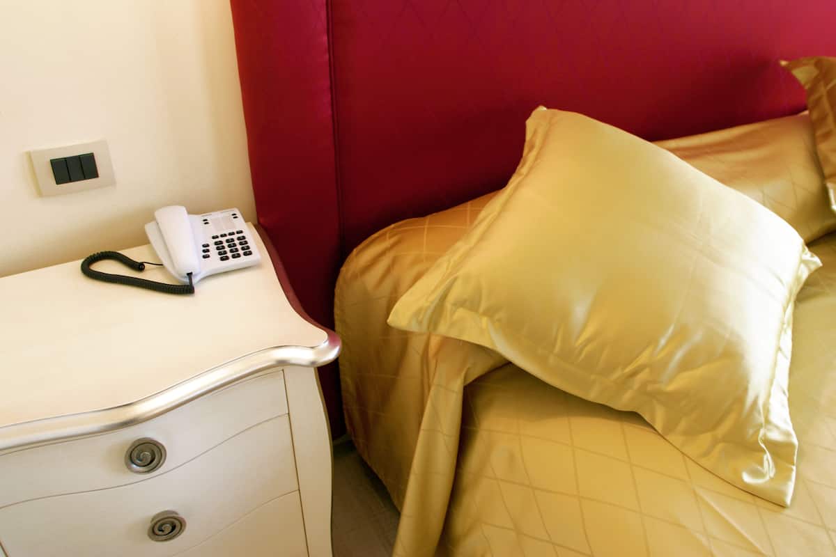 A hotel room with a bed, a bedside table with a telephone, and a red wall.