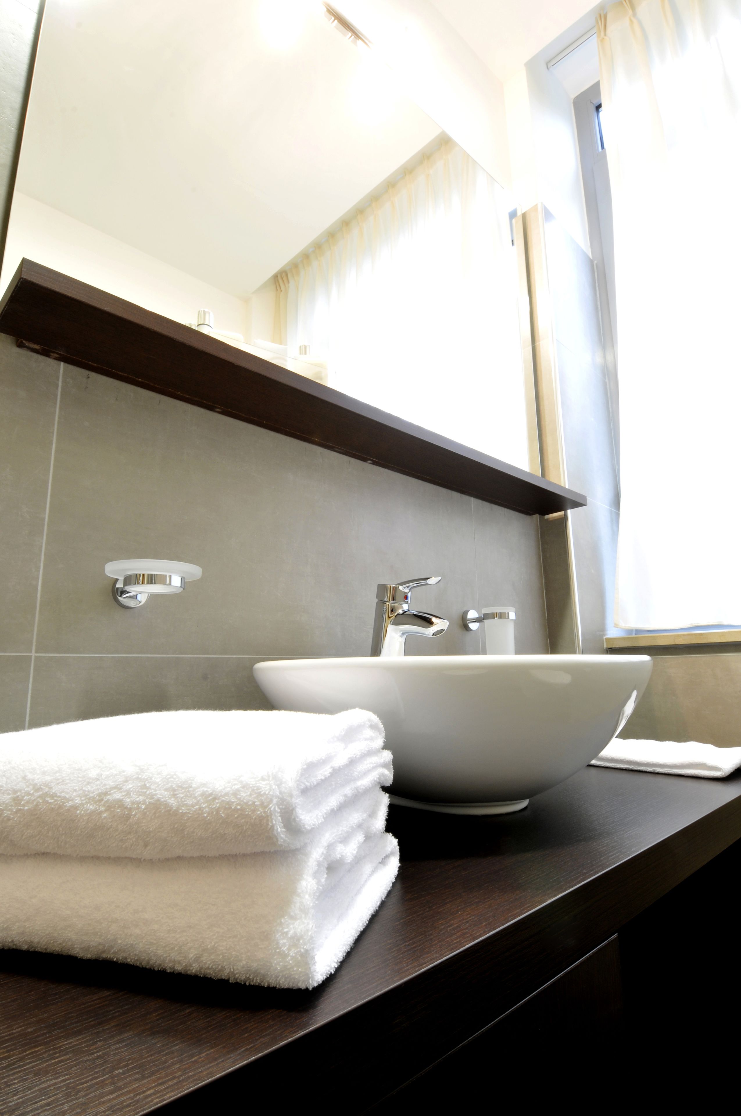 A bathroom with a white sink, a towel stack, and a mirror above the sink.